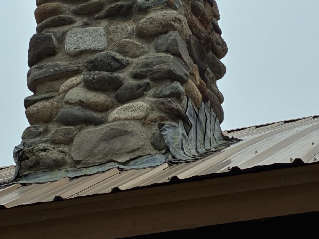 Corrugated metal roof meeting a stone chimney